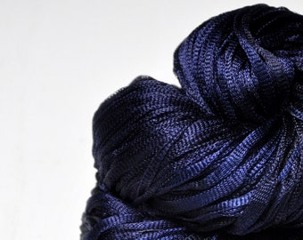 May include: A close-up of a bundle of navy blue fabric, tightly woven with a ribbed texture. The fabric has a slight sheen, and the folds create shadows that highlight the texture. The background is plain white.