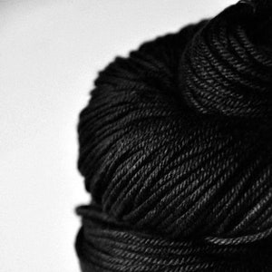 May include: A close-up shot of a tightly wound ball of black yarn. The yarn is textured, with visible strands creating a spiral pattern. The background is a plain white, emphasizing the yarn's dark color and texture. Ideal for knitting and crochet projects.
