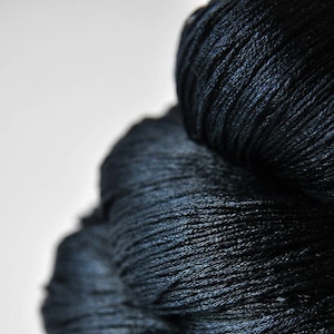 May include: A skein of deep navy blue yarn with a smooth, lustrous finish. The fibers are tightly twisted and bundled together, creating a dense, textured appearance with subtle highlights reflecting off the surface of the dark, saturated threads.