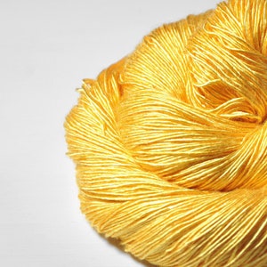 May include: A skein of bright yellow yarn, made of a soft, silky material. The yarn is tightly wound and has a smooth, even texture.