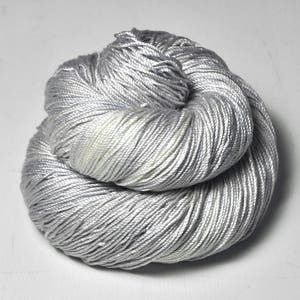 May include: A skein of silver gray yarn with a subtle shimmer. The yarn is made of a soft, smooth fiber and is perfect for knitting or crocheting.