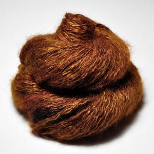 May include: A close-up shot of a ball of brown yarn with golden highlights. The yarn appears soft and textured, with varying shades of brown and a slight sheen. The yarn is likely used for knitting or crocheting projects.