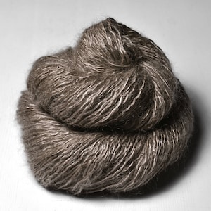 Könnte beinhalten: Ein Knäuel braunes Garn mit einem dezenten Schimmer. Das Garn ist weich und flauschig und perfekt zum Stricken oder Häkeln.