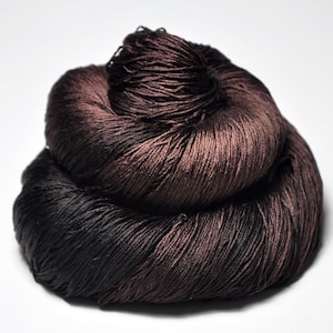 May include: A skein of dark brown yarn with a distinct sheen and smooth texture. The yarn is wound into a compact, layered coil, showcasing deep chocolate and espresso tones that reflect light across the twisted fibers of the material.