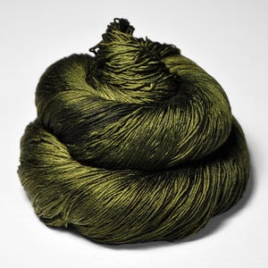 May include: A skein of olive green yarn with dark green and black accents. The yarn is tightly wound, showing a textured surface. The color gradient creates depth and visual interest. Ideal for knitting, crocheting, or other fiber arts projects.