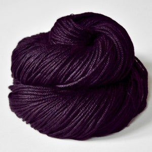 May include: A skein of dark purple yarn, tightly wound and textured. The yarn is a deep, rich color, appearing almost black in some areas. The fibers are closely packed, suggesting a smooth, high-quality material suitable for knitting or crocheting projects.