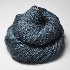 May include: A skein of dark blue yarn, made of a blend of silk and linen, is shown in a close-up view. The yarn is soft and textured, with a subtle sheen.