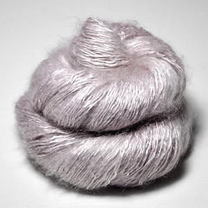 May include: A ball of soft, light gray yarn. The yarn appears to be a blend of fibers, with a slightly fuzzy texture and a subtle sheen. The fibers are tightly wound, creating a dense, yet airy appearance. Ideal for knitting or crocheting projects.