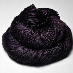 May include: A skein of dark purple yarn, tightly wound and textured. The yarn appears to have a slight sheen, reflecting light. The yarn is a deep, rich color, suitable for knitting or crocheting projects.