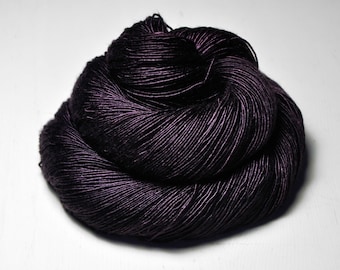 May include: A skein of dark purple yarn, tightly wound and textured. The yarn appears to have a slight sheen, reflecting light. The yarn is a deep, rich color, suitable for knitting or crocheting projects.