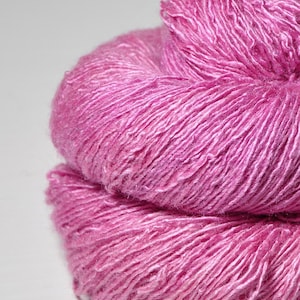 Könnte beinhalten: Nahaufnahme eines Strangs leuchtend rosa Garns. Das Garn ist eng gewickelt und zeigt eine strukturierte Oberfläche mit sichtbaren Strängen. Die Farbe ist ein helles, sattes Rosa, geeignet für Strick- oder Häkelprojekte.