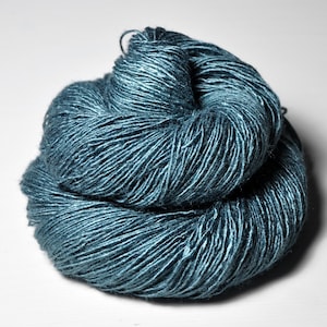 May include: A skein of teal-colored yarn, tightly wound and textured. The yarn appears to have a slight sheen, reflecting light. The image is a close-up, highlighting the individual strands and the overall shape of the yarn.