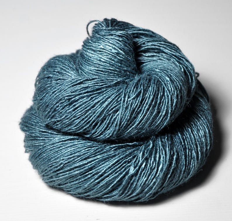 May include: A skein of teal-colored yarn, tightly wound and textured. The yarn appears to have a slight sheen, reflecting light. The image is a close-up, highlighting the individual strands and the overall shape of the yarn.