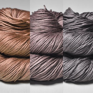 Könnte beinhalten: Fünf Garnknäuel in einer Farbverlaufsreihe von hellbeige bis dunkelgrau. Das Garn ist eng gewickelt und zeigt die Textur der Fasern. Ideal für Strick- oder Häkelprojekte.