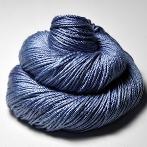 May include: A skein of soft, blue yarn, wound into a neat coil. The yarn is a light, dusty blue color and has a smooth, silky texture.