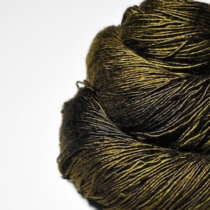 May include: Close-up of a skein of yarn, featuring a blend of olive green and black fibers. The yarn is tightly wound, showcasing a textured surface and a gradient effect from dark to lighter shades. Ideal for knitting or crochet projects.
