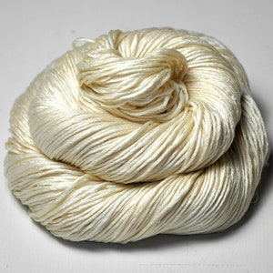 May include: A close-up of a large bundle of off-white yarn. The yarn is soft and fluffy, and it is arranged in a loose, circular shape.