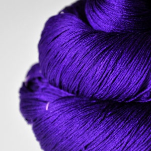 May include: A close-up of a vibrant purple yarn skein. The yarn is tightly wound, revealing fine strands and a textured surface. The deep violet color is prominent against a white background, suggesting a craft supply for knitting or crochet projects.