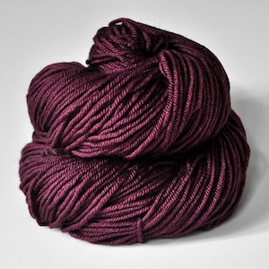 May include: A close-up shot of a skein of burgundy-colored yarn. The yarn is tightly wound, showing individual strands. The yarn is a deep, rich shade of red-purple, with a slight sheen. The yarn is likely used for knitting or crocheting projects.