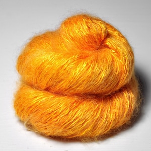 May include: A skein of bright orange yarn, made of a blend of silk and mohair, with a soft, fuzzy texture.