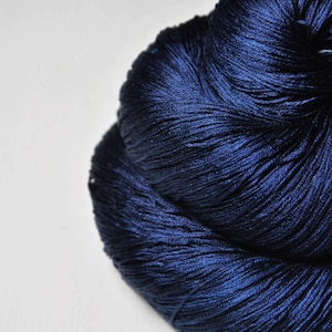 May include: A large, tightly wound ball of navy blue yarn. The yarn has a subtle sheen, suggesting a high-quality fiber. The texture appears soft and pliable, ideal for knitting or crocheting projects. The yarn is set against a plain white background.