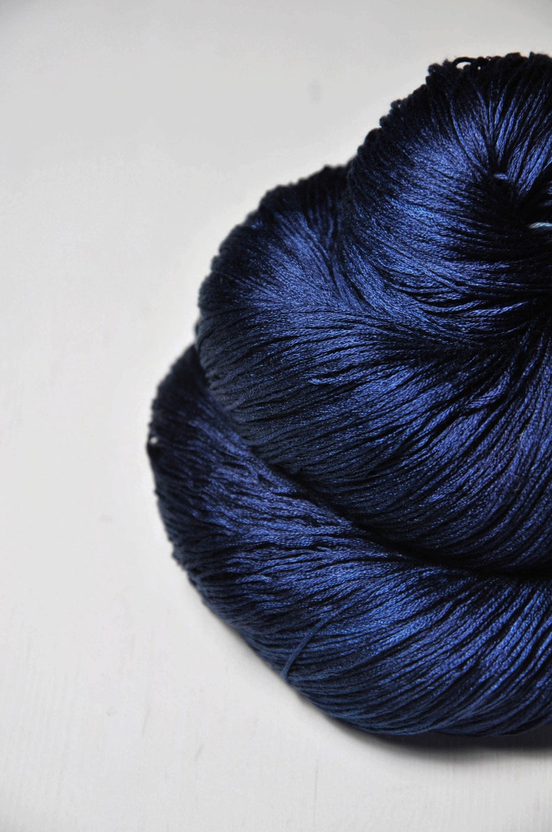 May include: A large, tightly wound ball of navy blue yarn. The yarn has a subtle sheen, suggesting a high-quality fiber. The texture appears soft and pliable, ideal for knitting or crocheting projects. The yarn is set against a plain white background.