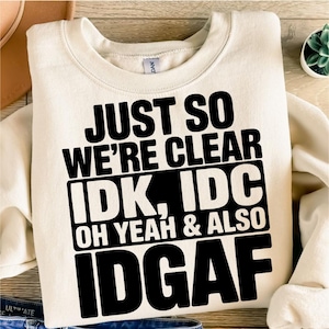 以下が含まれることがあります： クリーム色のスウェットシャツに、黒い文字で「Just so we're clear IDK, IDC Oh yeah & also IDGAF」と書かれています。