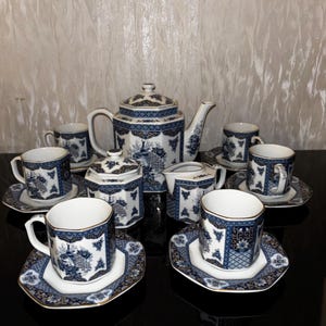 Könnte beinhalten: Ein blaues und weißes Porzellan-Tee-Set mit einer Teekanne, einer Zuckerdose, einem Milchkännchen und sechs Tassen und Untertassen. Das Set zeigt ein florales Design mit goldenen Akzenten.