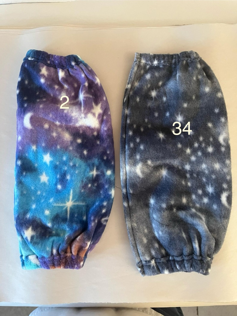 Pode incluir: Dois pares de aquecedores de pernas de l&atilde; polar com estampa de gal&aacute;xia. Um par &eacute; azul, roxo e branco com o n&uacute;mero "2" nele. O outro par &eacute; cinza com o n&uacute;mero "34" nele.