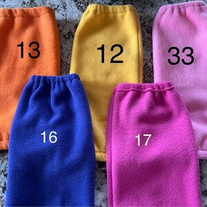 Pode incluir: Cinco aquecedores de pernas de l&atilde; polar em diferentes cores: laranja, amarelo, rosa, azul e rosa choque. Cada aquecedor tem um n&uacute;mero escrito nele: 13, 12, 33, 16 e 17.