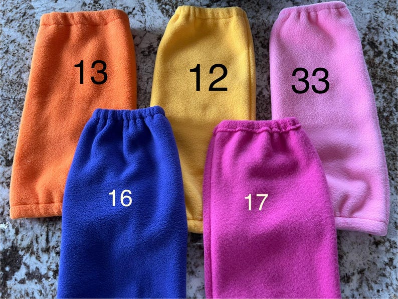 Pode incluir: Cinco aquecedores de pernas de l&atilde; polar em diferentes cores: laranja, amarelo, rosa, azul e rosa choque. Cada aquecedor tem um n&uacute;mero escrito nele: 13, 12, 33, 16 e 17.