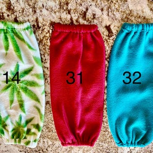 Pode incluir: Tr&ecirc;s aquecedores de bra&ccedil;o de l&atilde; polar, um com um padr&atilde;o de folhas de marijuana verde e branco, um vermelho e um azul turquesa. Os aquecedores de bra&ccedil;o s&atilde;o numerados 14, 31 e 32.