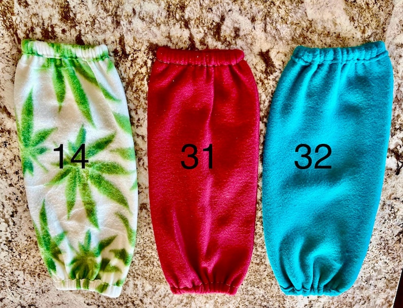 Pode incluir: Tr&ecirc;s aquecedores de bra&ccedil;o de l&atilde; polar, um com um padr&atilde;o de folhas de marijuana verde e branco, um vermelho e um azul turquesa. Os aquecedores de bra&ccedil;o s&atilde;o numerados 14, 31 e 32.
