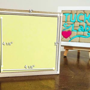 Puede incluir: Un marco cuadrado de madera con un inserto amarillo claro, que mide 12,7 cm por 12,7 cm en el exterior y 10,48 cm por 10,48 cm en el interior. Al fondo, un marco blanco sobre un caballete muestra el texto TUCK LAB.