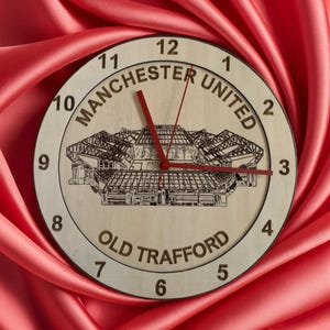 May include: A wooden clock featuring a black and white image of Old Trafford, the home of Manchester United. The clock face displays the words "Manchester United" and "Old Trafford". The clock hands are red.