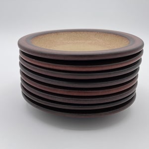 May include: A stack of ceramic plates with a brown rim and a tan interior. The plates have a layered design with varying shades of brown and are stacked on top of each other. The plates are likely for serving food.