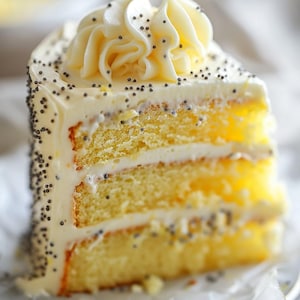 May include: A slice of layered cake with yellow sponge cake and white frosting. The frosting is decorated with poppy seeds and a swirl on top. The cake sits on a piece of white parchment paper.