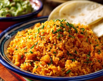 Op de afbeelding: Een kom met levendige oranje Mexicaanse rijst, gegarneerd met verse bieslook, staat naast een kom guacamole en een stapel tortilla's. De kom heeft een blauw-witte rand. De scène is geplaatst op een kleurrijke, bedrukte doek.