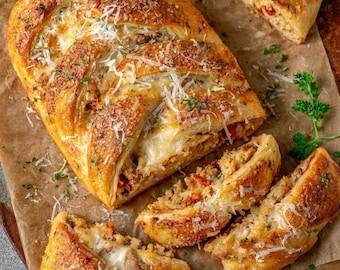 May include: A golden-brown, braided bread loaf, sliced to reveal a savory filling. The bread is topped with grated cheese and herbs. Several slices are arranged around the loaf on a brown surface, showcasing the filling's texture and ingredients.