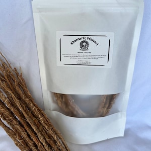 Puede incluir: Una bolsa blanca resellable con una ventana transparente que muestra raíces de vetiver marrones. La bolsa tiene una etiqueta que dice "Khamarté (Vetiver) 100% Bio. Naturelle Jana"