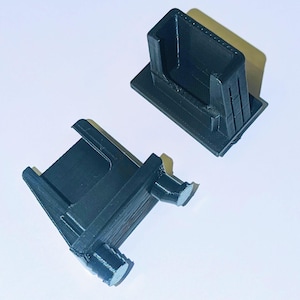 以下が含まれることがあります： 黒い長方形のプラスチック部品が2つ。1つは箱のような構造と円筒形の突起があり、もう1つはより開いています。これらの部品は組み合わされるように設計されています。