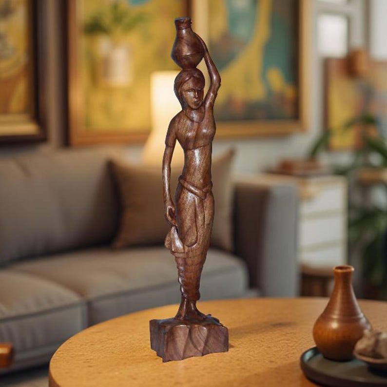 May include: A wooden sculpture of a woman carrying a water jug on her head. The figure is carved from dark brown wood and stands on a square base. The sculpture is a decorative item.