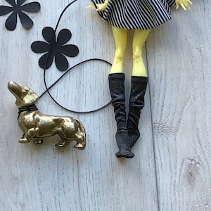 May include: A gold-colored dachshund figurine with a black leash attached to a doll wearing a black and white striped dress and black boots.