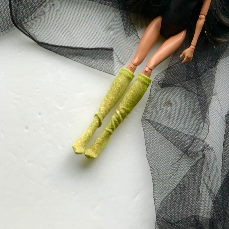 May include: A pair of lime green sparkly knee-high socks. The socks are on a doll's legs.