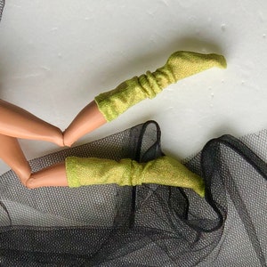 May include: A pair of lime green sparkly doll socks with a ribbed texture. The socks are on a black mesh fabric.