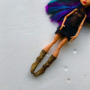 May include: A doll with long, purple and blue hair wearing a black mesh dress and gold sparkly socks.