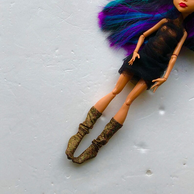 May include: A doll with long, purple and blue hair wearing a black mesh dress and gold sparkly socks.
