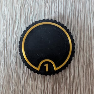 May include: Black and gold circular token with the number "1" in a gold arch.