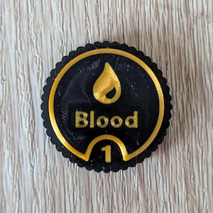 Puede incluir: Ficha negra y dorada con una gota de sangre dorada y la palabra "Blood" en letras doradas. La ficha también tiene el número "1" en dorado.