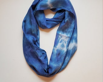 May include: A blue silk infinity scarf with a tie-dye pattern. The scarf is folded in a loop and has a white background with blue swirls.